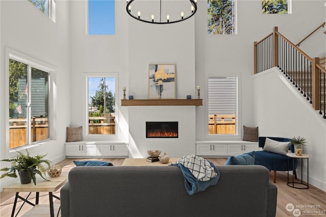 living room with a towering ceiling, light hardwood / wood-style floors, a notable chandelier, and a brick fireplace