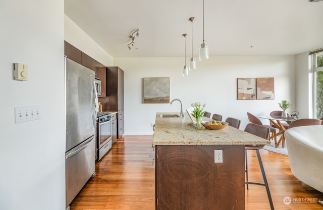 kitchen featuring sink, stainless steel appliances, pendant lighting, a kitchen island with sink, and a breakfast bar