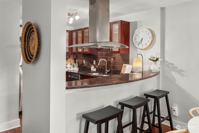 kitchen featuring sink, tasteful backsplash, kitchen peninsula, island exhaust hood, and dark stone counters