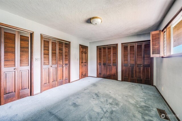 unfurnished bedroom featuring carpet floors, two closets, and a textured ceiling