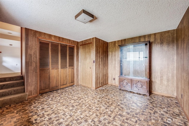 unfurnished bedroom with parquet flooring, a closet, a textured ceiling, and wood walls