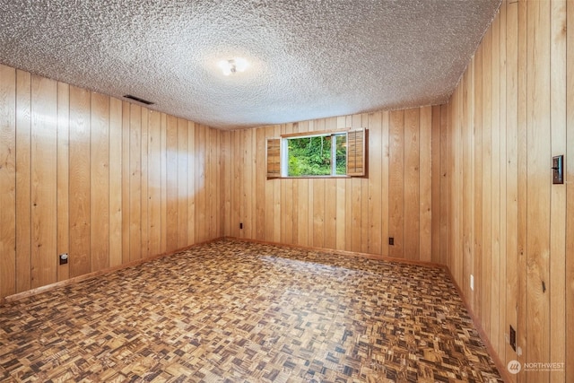 unfurnished room with dark parquet flooring, a textured ceiling, and wood walls