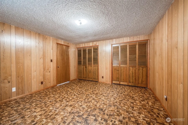 spare room with parquet flooring, a textured ceiling, and wood walls