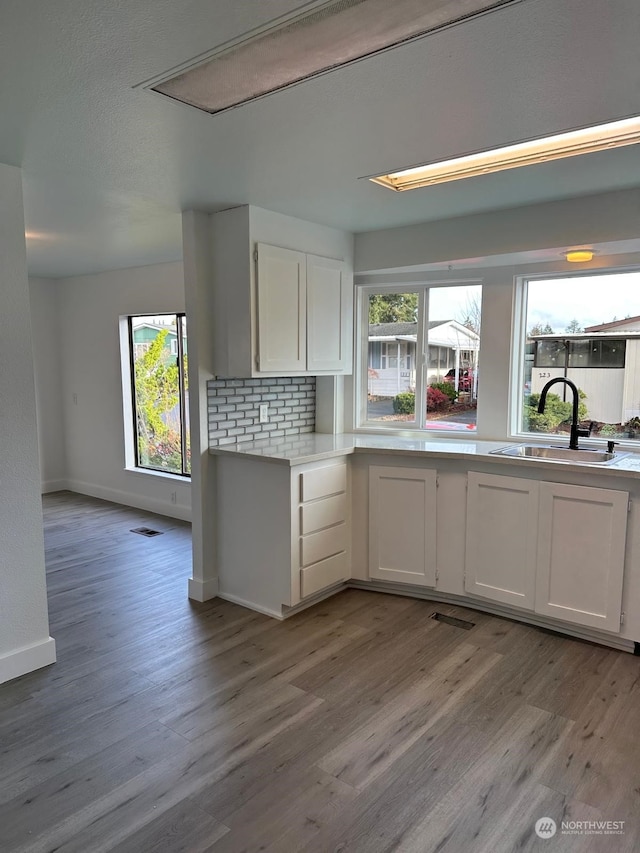 kitchen with tasteful backsplash, white cabinetry, sink, and light hardwood / wood-style floors