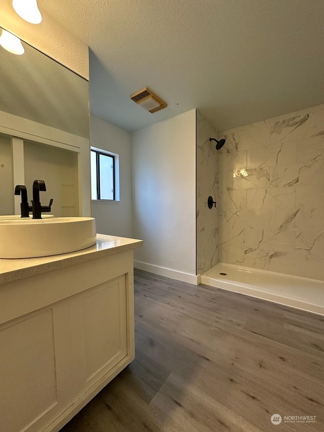 bathroom featuring vanity, a tile shower, wood-type flooring, and a textured ceiling