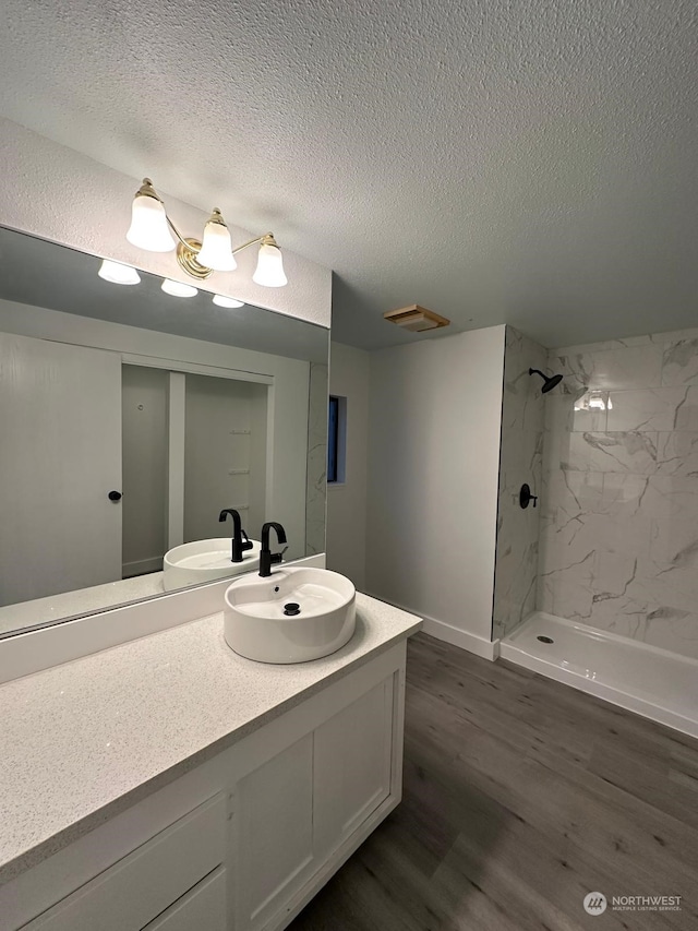 bathroom featuring hardwood / wood-style floors, vanity, a tile shower, and a textured ceiling