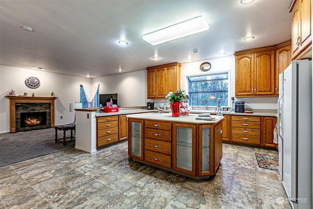 kitchen featuring white refrigerator with ice dispenser, carpet flooring, a fireplace, a kitchen island, and kitchen peninsula