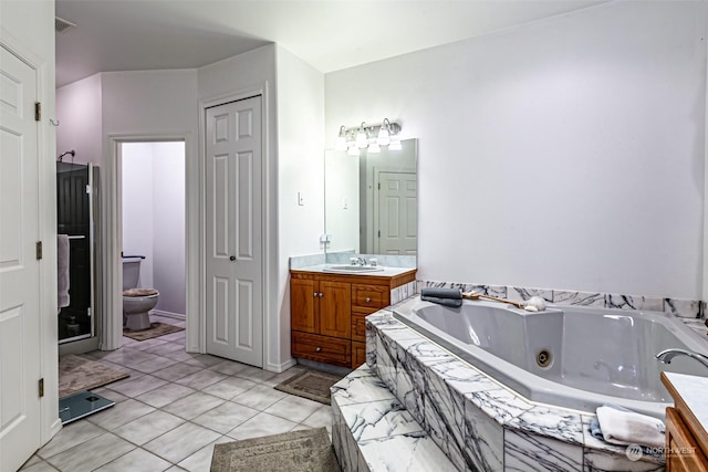 bathroom with tile patterned floors, vanity, a relaxing tiled tub, and toilet