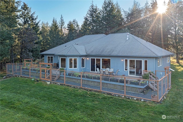 rear view of property featuring roof with shingles and a lawn