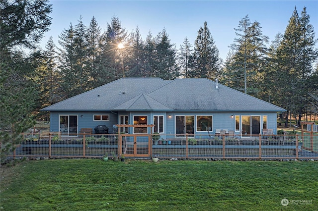 back of property featuring a shingled roof, fence, and a yard