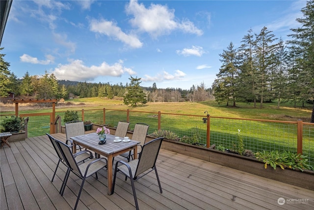 wooden terrace featuring outdoor dining space, a rural view, and a yard