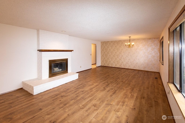 unfurnished living room with hardwood / wood-style flooring, a notable chandelier, a textured ceiling, and a brick fireplace