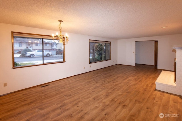 unfurnished living room featuring a fireplace, a chandelier, a textured ceiling, and hardwood / wood-style flooring