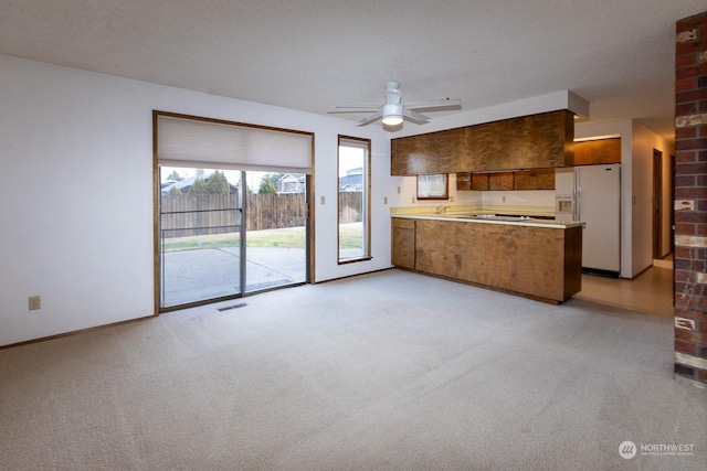 kitchen with ceiling fan, white fridge with ice dispenser, a textured ceiling, light colored carpet, and kitchen peninsula