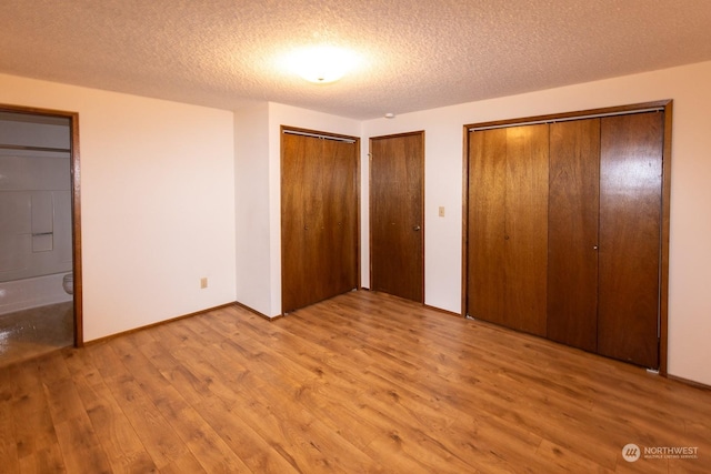 unfurnished bedroom featuring a textured ceiling, ensuite bathroom, light hardwood / wood-style flooring, and two closets