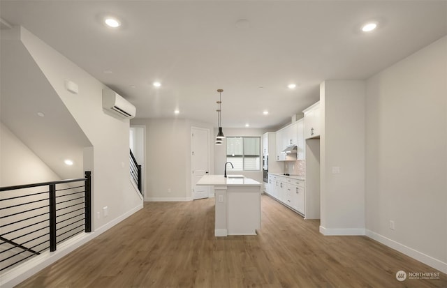 kitchen with sink, white cabinetry, a kitchen island with sink, and a wall mounted air conditioner