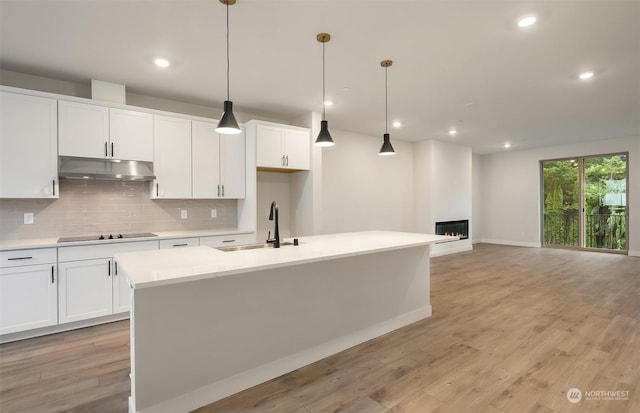 kitchen with hanging light fixtures, sink, white cabinetry, a kitchen island with sink, and black electric cooktop