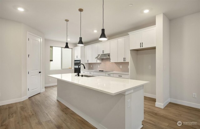 kitchen featuring black appliances, hanging light fixtures, sink, white cabinets, and a center island with sink