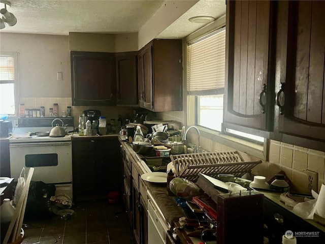 kitchen with dark tile patterned floors, a textured ceiling, decorative backsplash, dark brown cabinets, and range