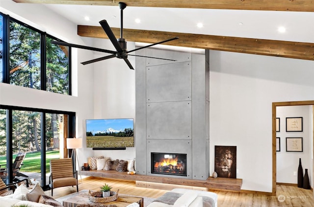 living room featuring light wood-type flooring, a fireplace, ceiling fan, beamed ceiling, and a high ceiling