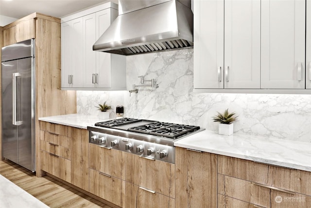 kitchen featuring tasteful backsplash, light stone counters, wall chimney exhaust hood, stainless steel appliances, and white cabinetry