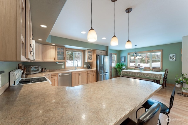 kitchen with a breakfast bar, sink, light brown cabinetry, decorative light fixtures, and stainless steel appliances