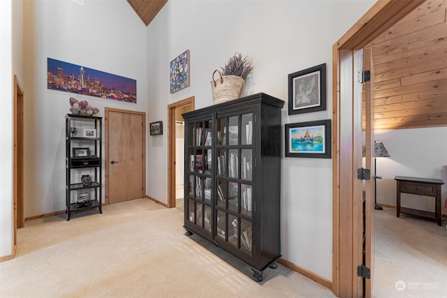 hall with light colored carpet, wood ceiling, and high vaulted ceiling