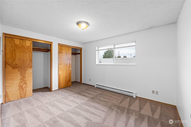 unfurnished bedroom featuring a baseboard heating unit, a textured ceiling, multiple closets, and light carpet