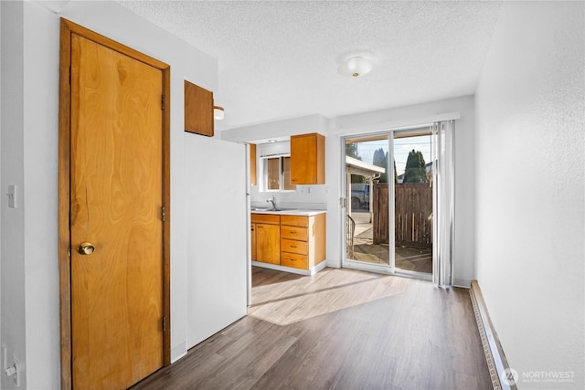 kitchen featuring brown cabinetry, wood finished floors, a sink, light countertops, and a textured ceiling