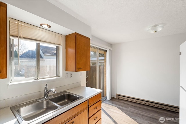 kitchen with brown cabinetry, light wood-style flooring, a sink, light countertops, and a baseboard heating unit