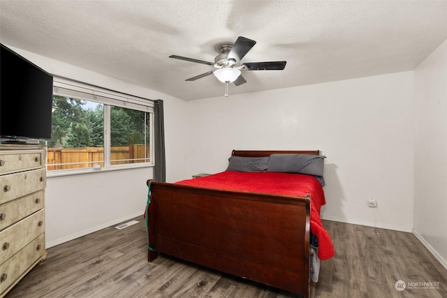 bedroom with a textured ceiling, ceiling fan, and dark wood-type flooring