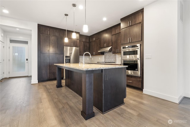 kitchen with dark brown cabinetry, sink, a kitchen breakfast bar, a center island with sink, and appliances with stainless steel finishes