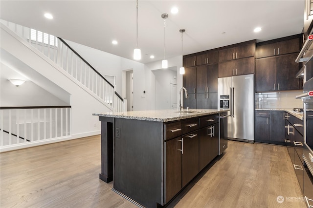 kitchen featuring appliances with stainless steel finishes, light wood-type flooring, dark brown cabinetry, a kitchen island with sink, and sink