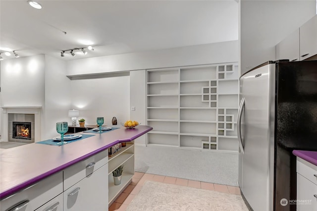 kitchen featuring stainless steel fridge, track lighting, white cabinets, light tile patterned flooring, and a tiled fireplace