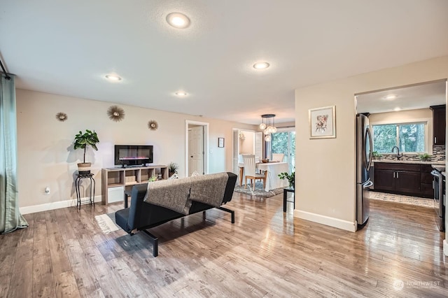 living room with sink, a notable chandelier, and light hardwood / wood-style flooring