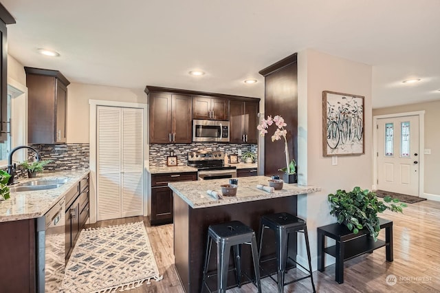 kitchen with light stone countertops, sink, light wood-type flooring, and appliances with stainless steel finishes