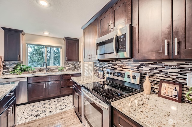 kitchen with sink, stainless steel appliances, light stone counters, light hardwood / wood-style flooring, and dark brown cabinets