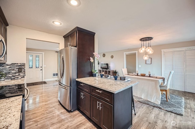 kitchen featuring hanging light fixtures, decorative backsplash, stainless steel fridge, light stone countertops, and a kitchen bar