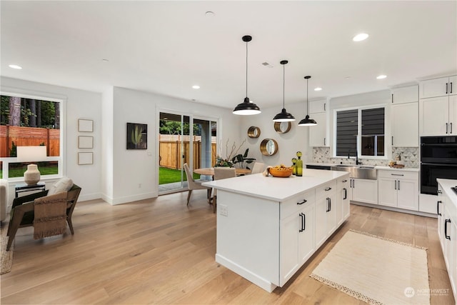 kitchen featuring decorative light fixtures, backsplash, white cabinetry, and a center island