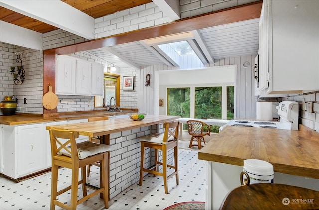 kitchen with butcher block counters, a skylight, electric range oven, a wealth of natural light, and white cabinets