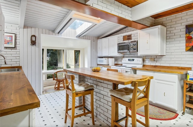 kitchen with lofted ceiling with skylight, butcher block counters, sink, white cabinetry, and white appliances