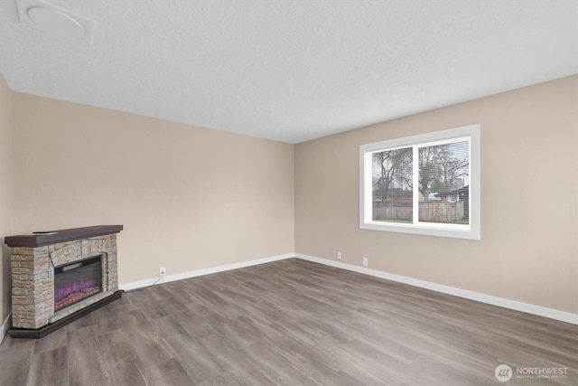 unfurnished living room featuring a textured ceiling, a stone fireplace, baseboards, and wood finished floors