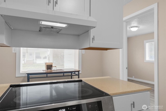 kitchen featuring electric stove, light countertops, white cabinets, under cabinet range hood, and baseboards