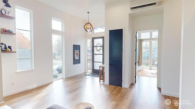 entryway with an AC wall unit, a wealth of natural light, light hardwood / wood-style floors, and a notable chandelier