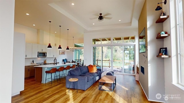 living room featuring plenty of natural light, ceiling fan, a raised ceiling, and light hardwood / wood-style floors