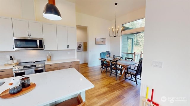 kitchen with pendant lighting, backsplash, an inviting chandelier, white cabinetry, and stainless steel appliances