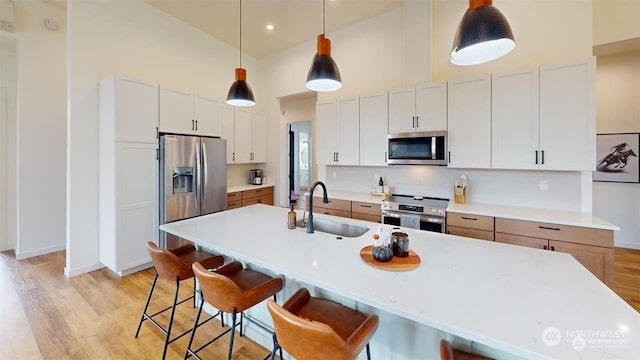 kitchen with a kitchen island with sink, sink, appliances with stainless steel finishes, decorative light fixtures, and white cabinetry