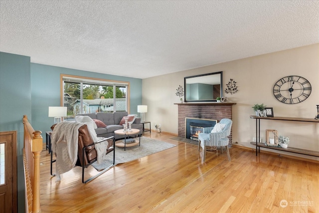 living room featuring light hardwood / wood-style flooring, a textured ceiling, and a brick fireplace