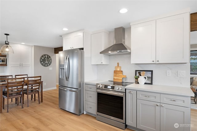 kitchen with stainless steel appliances, wall chimney range hood, pendant lighting, light hardwood / wood-style floors, and white cabinetry