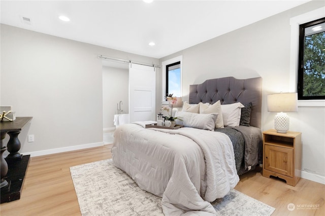 bedroom with a barn door and light hardwood / wood-style flooring